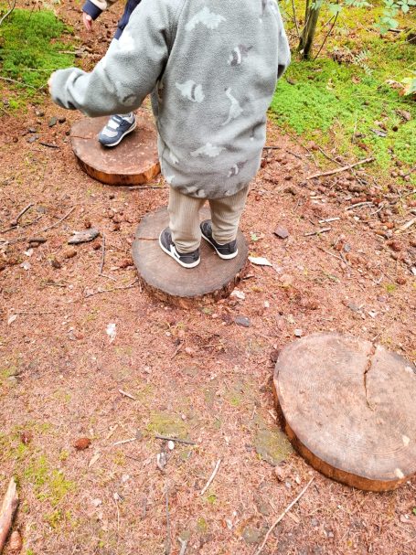 naturnahe Bildung Ein Kind balanciert auf Baumstümpfen im Wald.